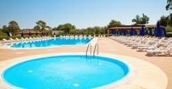 Due piscine rotonde, circondate da lettini bianchi e ombrelloni blu.
