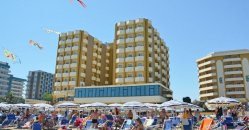 Spiaggia affollata con ombrelloni e un grande hotel sullo sfondo.