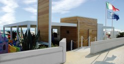 Struttura moderna in legno con bandiere sventolanti e una spiaggia vicina.