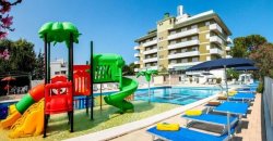 Piscina con scivoli colorati e lettini sotto ombrelloni, accanto a un edificio.