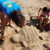 Bambini costruiscono una tartaruga di sabbia sulla spiaggia.