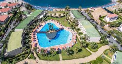 Vista aerea di un grande resort con piscina centrale e giardini, vicino al mare.