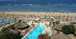 Spiaggia e piscina affollate con ombrelloni.