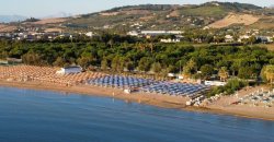 Spiaggia con ombrelloni blu e colline sullo sfondo.