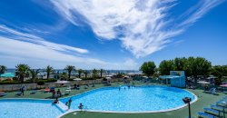 Piscina all'aperto con persone che nuotano, cielo parzialmente nuvoloso.
