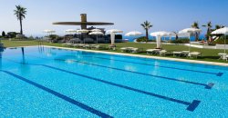 Piscina con corsie, ombrelloni bianchi e vista sul mare.