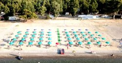Spiaggia con lettini e ombrelloni verdi disposti in file ordinate.