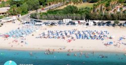 Una spiaggia affollata con ombrelloni blu e bianchi e persone in acqua.