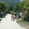 Tre persone con biciclette su un vialetto di ghiaia, circondati da bungalow e vegetazione.
