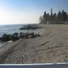 Spiaggia di ciottoli con massi, lambita da un lago, circondata da alberi.