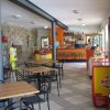 Un bar accogliente con tavoli e sedie nere, bancone arancione e frigo Coca-Cola.