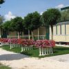 Mobilhome con terrazza fiorita, alberi e vialetto di ghiaia.