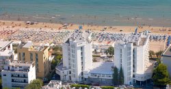 Complesso di edifici bianchi vicino a una spiaggia affollata di ombrelloni colorati.