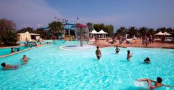 Una piscina affollata con persone che nuotano e scivoli in background.