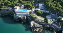 Complesso alberghiero su una scogliera, con piscina e pini circostanti.