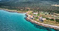 Veduta aerea di una costa rocciosa con mare turchese e costruzioni sparse sul promontorio.