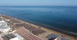 Spiaggia con file di ombrelloni e mare calmo all'orizzonte.