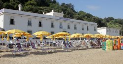 Spiaggia con sdraio e ombrelloni gialli davanti a un hotel.