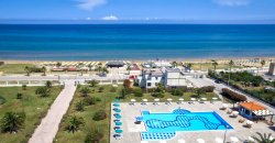 Piscina azzurra con lettini, prato e spiaggia sullo sfondo.