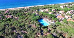 Complesso turistico immerso nel verde con piscina e spiaggia sullo sfondo.